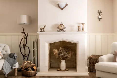 A white fireplace and mirror beside an armchair in the Farmhouse